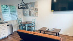 Una sala moderna con un sofá, una mesa de comedor con sillas, una pequeña cocina y un televisor de pantalla plana montado en la pared.