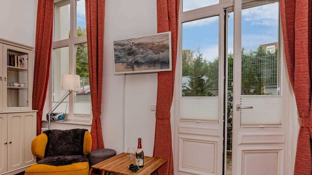 Ein gemütliches Wohnzimmer mit einem gelben Sessel, einem kleinen Tisch mit Flasche und Gläsern sowie einem Bild an der Wand.