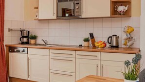 Eine moderne Küche mit weißen Schränken, einer Holz Arbeitsplatte, einer Kaffeemaschine, einem Wasserkocher und einer Obstschale.