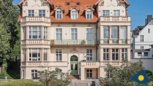 Ein großes, verziertes Gebäude mit einem zentralen Eingang, zahlreichen Fenstern und einem roten Ziegeldach.