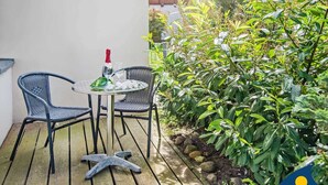 Eine Terrasse mit zwei Korbstühlen und einem runden Tisch, einer Champagnerflasche und zwei Gläsern.