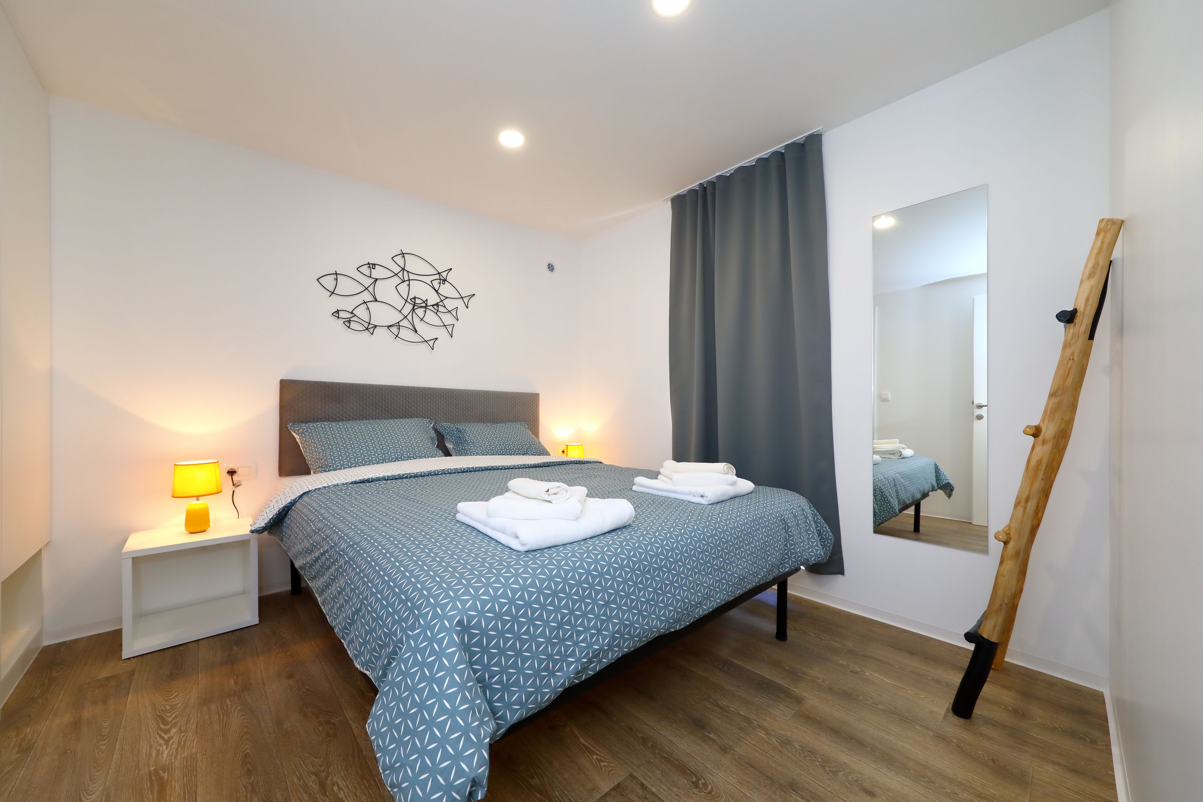 Ein modernes Schlafzimmer mit einem Bett, Nachttischlampen, Holzboden, einem Wandspiegel und einem Gemälde.