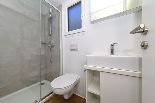 A modern bathroom with a glass shower enclosure, a white toilet, and a white sink with a mirror above it. - Pine Beach Mobile homes – all inclusive (Pakostane)