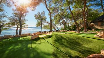 Um campo de golfe bem cuidado, com vista para o mar e montanhas ao fundo.