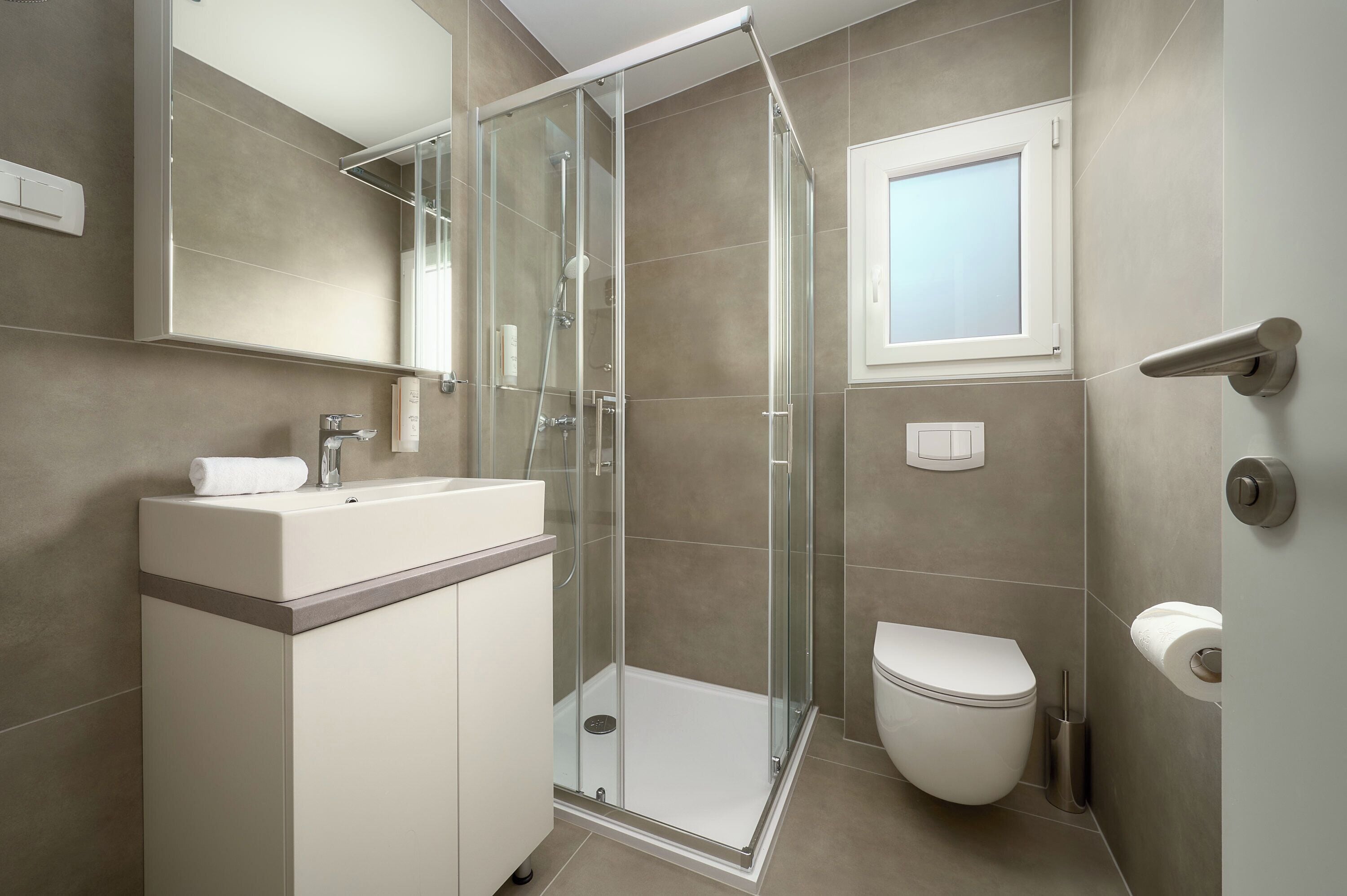 Een moderne badkamer met een douchecabine van glas, een toilet en een wastafel met spiegel erboven.