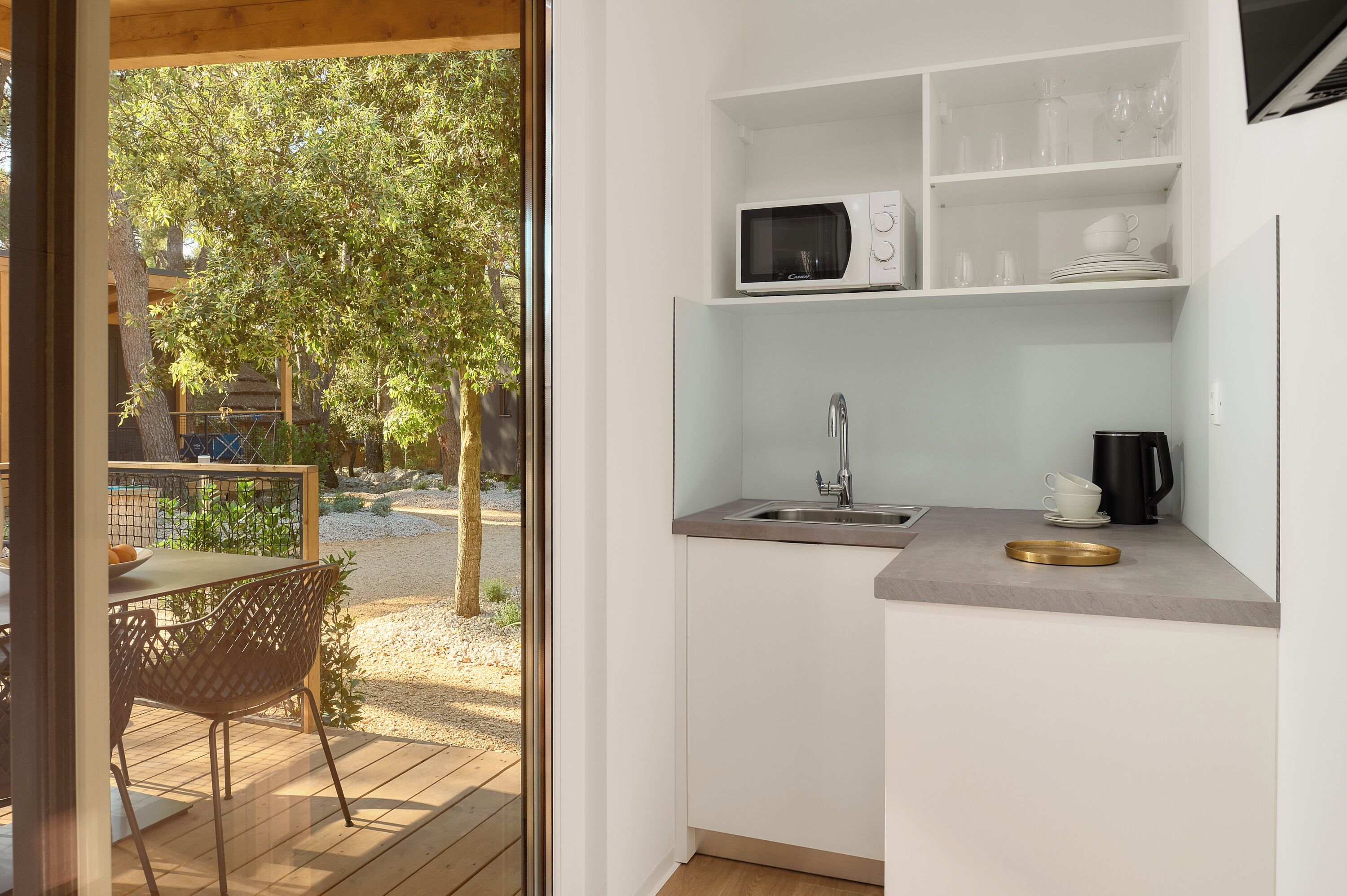 A compact kitchen with a sink, microwave, and shelves for dishes.