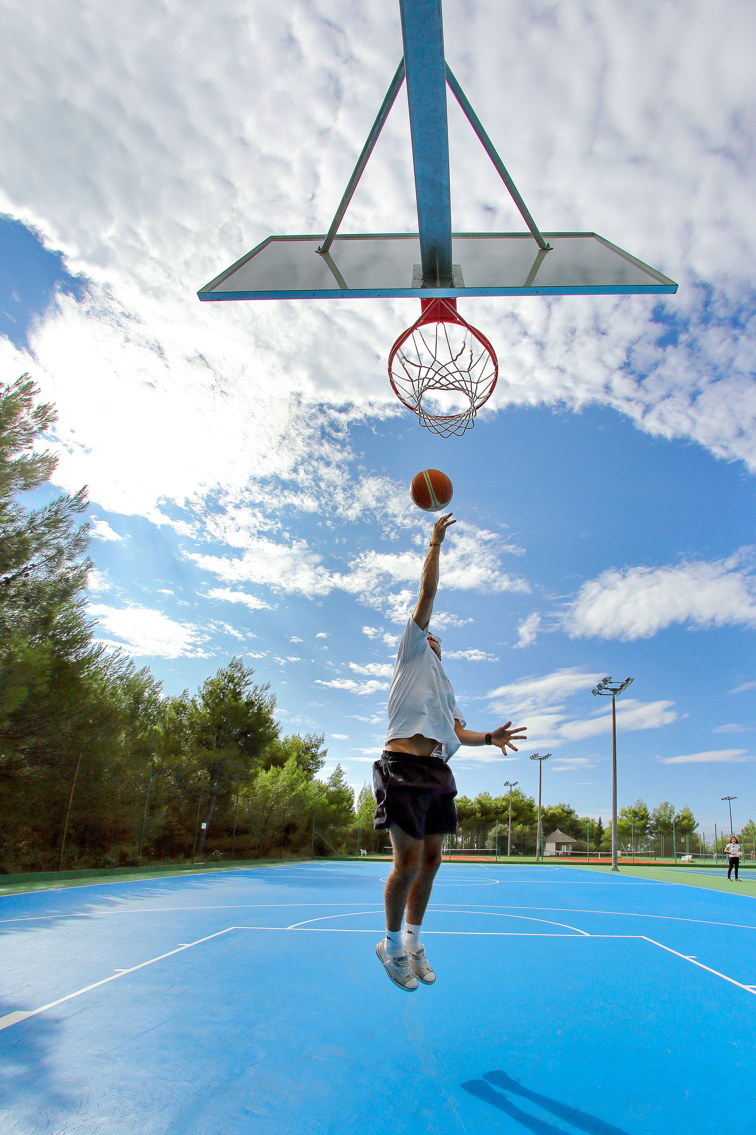 A basketball court with a hoop, trees, and a clear sky.