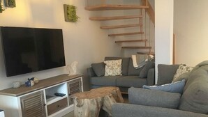 Uma sala de estar moderna com televisão de tela plana, sofá cinza, mesa de centro de madeira e uma escada.