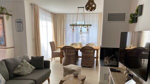 Uma sala de estar moderna com sofá, mesa de centro, área de jantar e televisão.