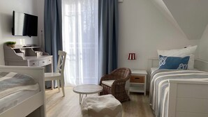 Quarto moderno e bem iluminado, com cama, escrivaninha, cadeira e mesinha.