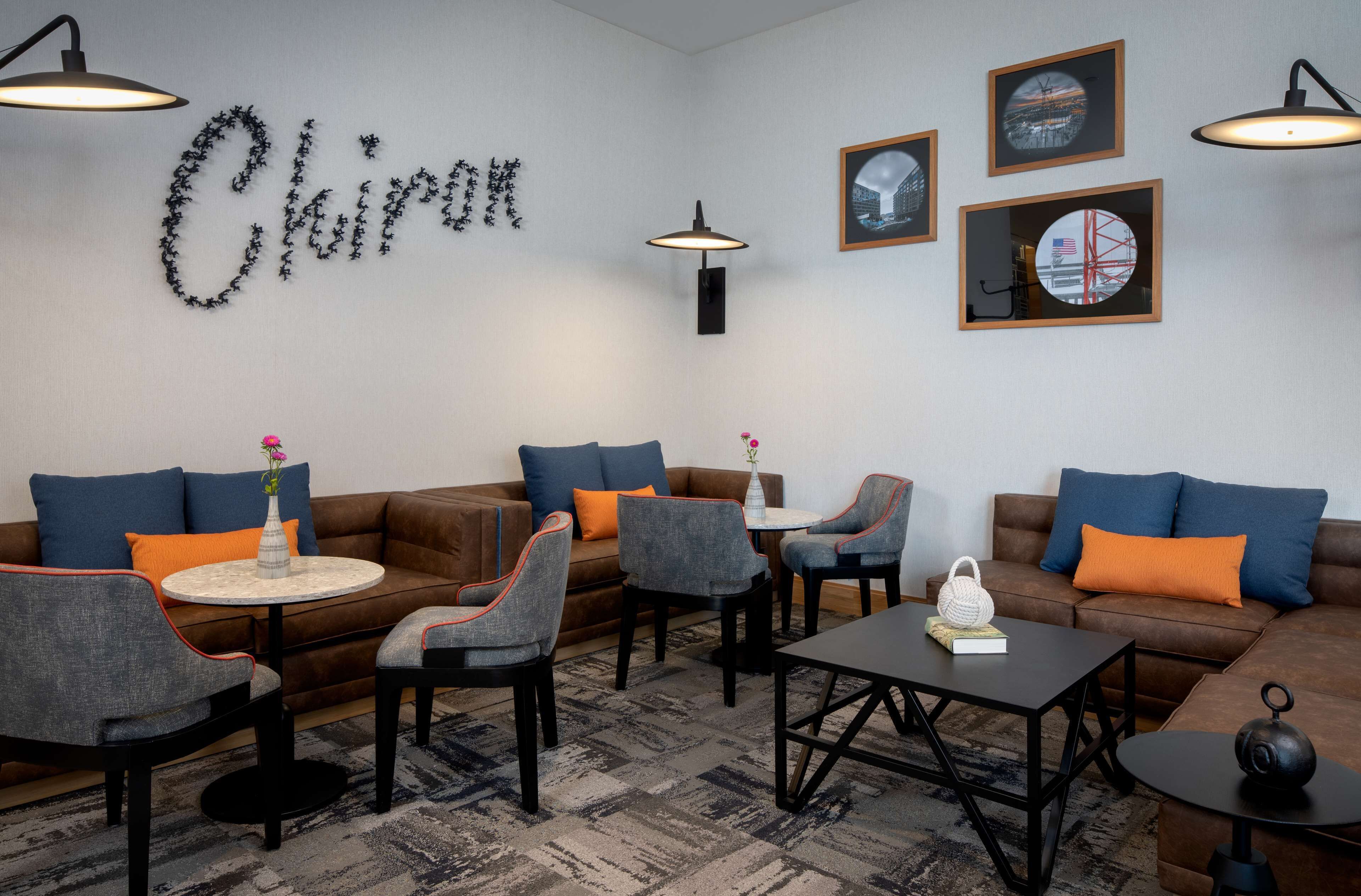 Ein stilvoller Lounge-Bereich mit einem braunen Sofa, grauen Sessel, einem runden Couchtisch und einem kleinen Tisch mit Blumen.