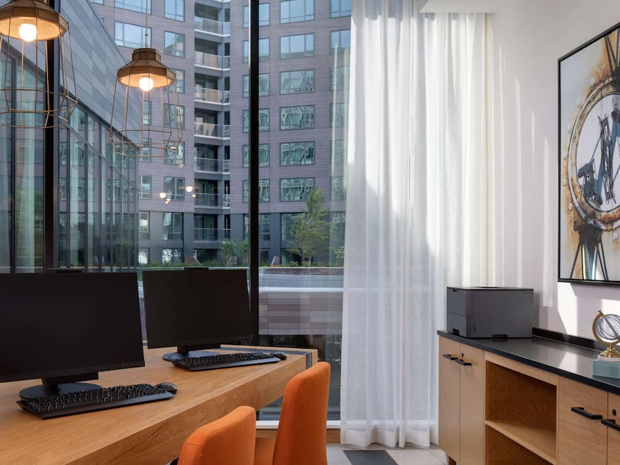 Un espacio de oficina moderno con dos monitores de ordenador, un escritorio de madera y sillas naranja.