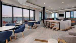 A modern lounge with large windows, a bar area, and seating arrangements. - Hyatt Place Boston/Seaport District (Boston)