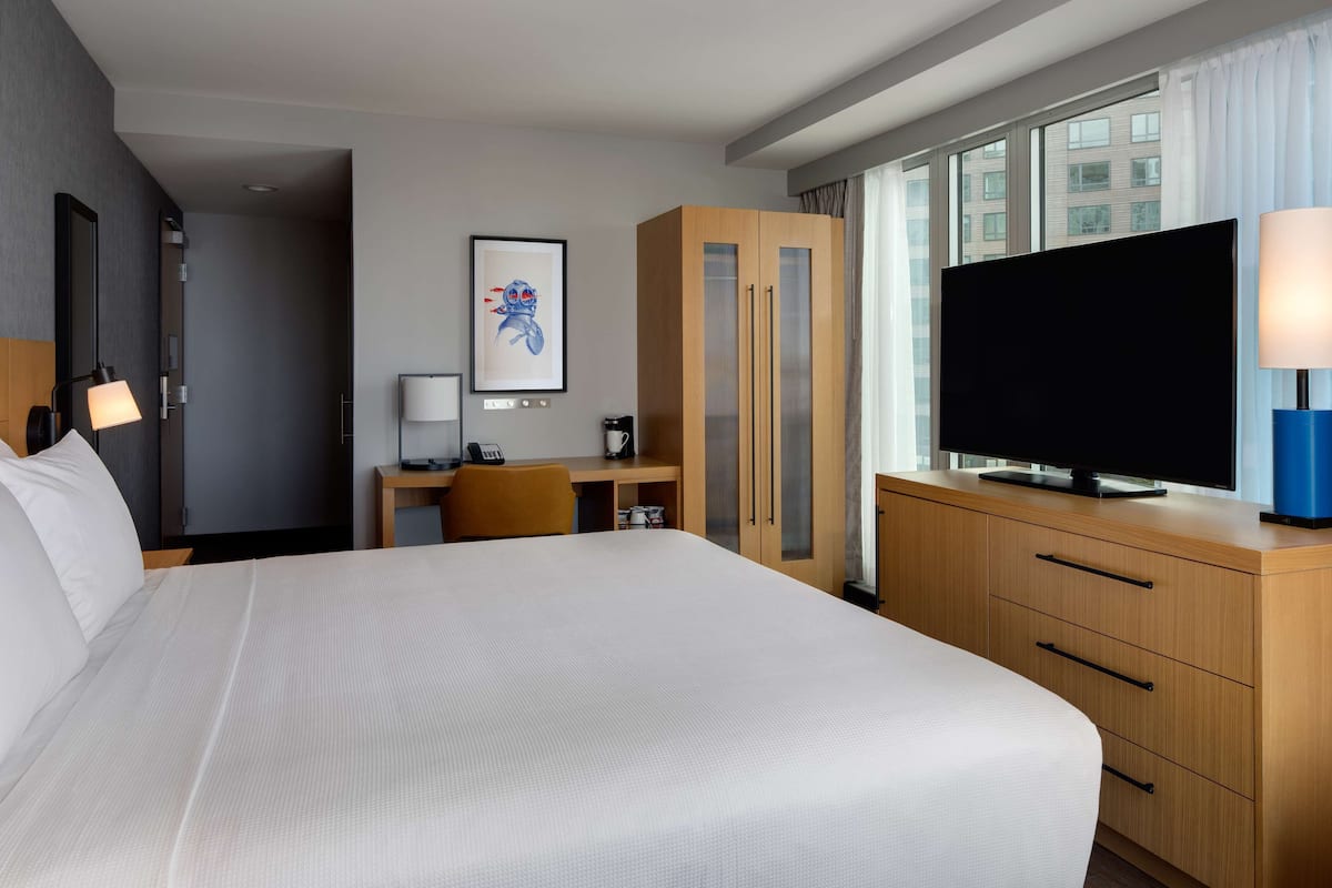 A hotel room with a large bed, a desk with a chair, a television, and a wardrobe.