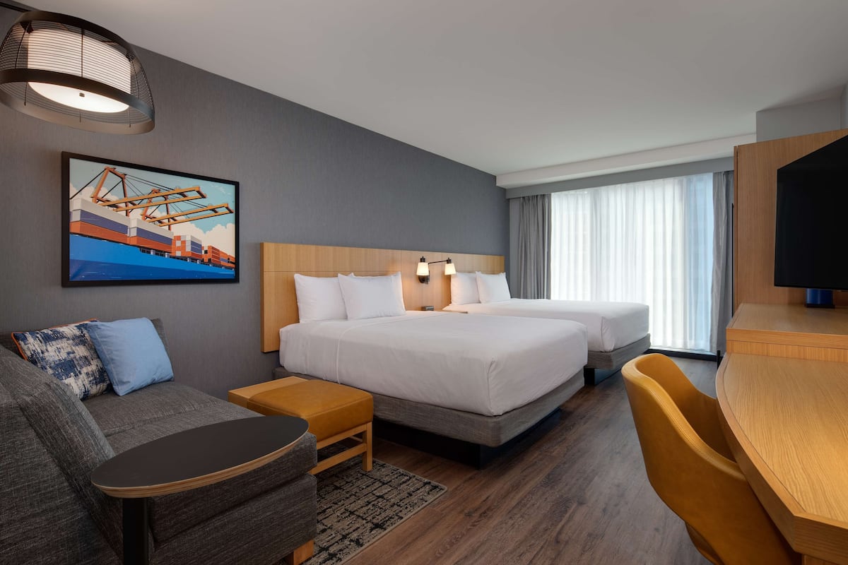 A hotel room with two beds, a sofa, a desk, and a television.