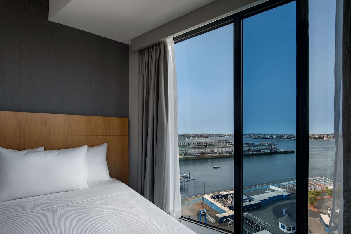 A hotel room with a large window offering a view of a waterfront and a bridge.