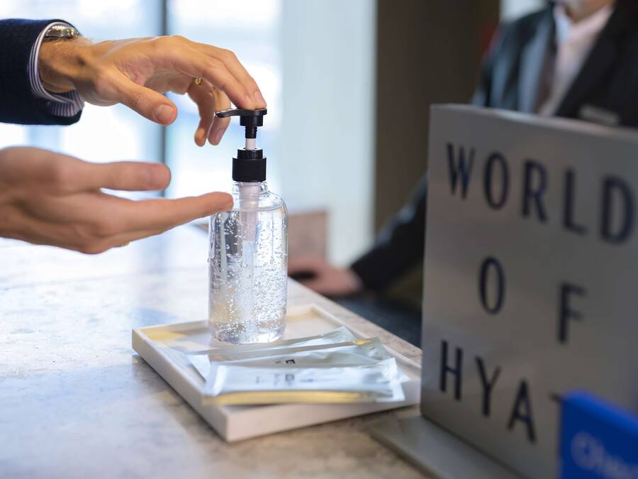 A hand using a hand sanitizer dispenser on a tray with a bottle, next to a sign reading "WORLD OF HYATT".