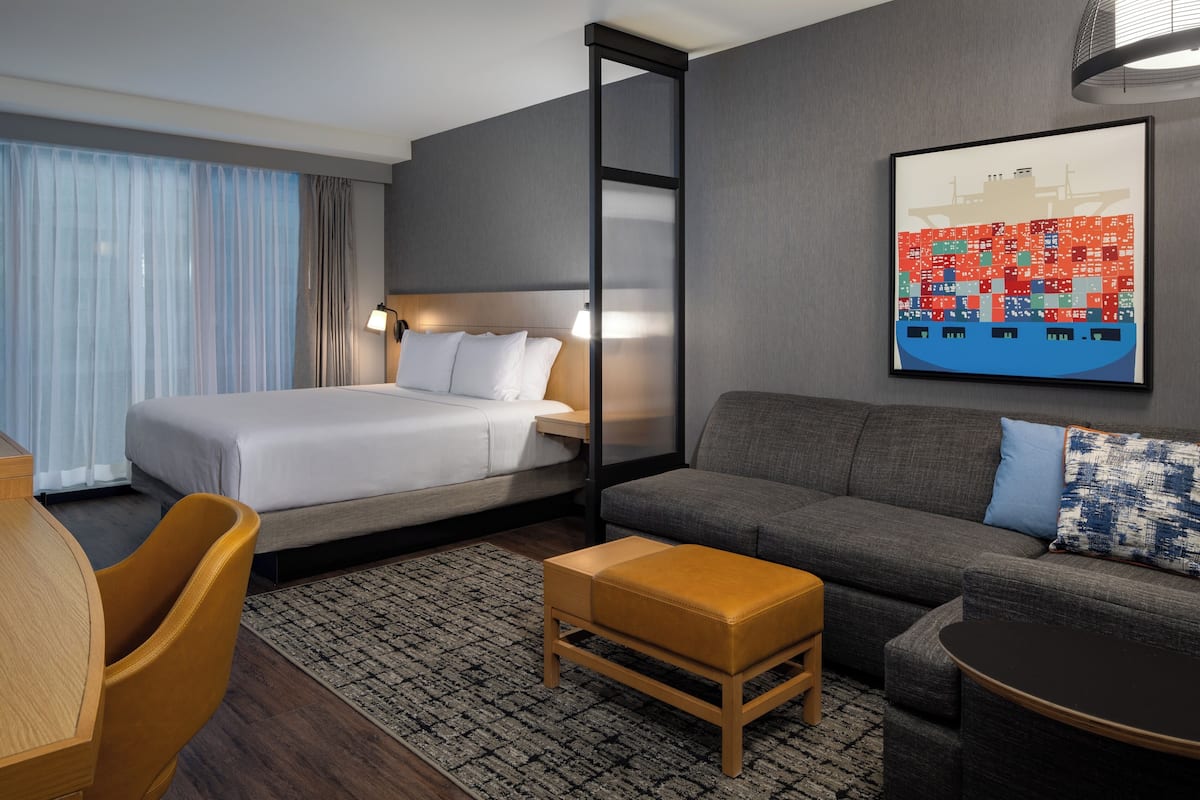 A hotel room with a bed, sofa, ottoman, and a table with chairs.