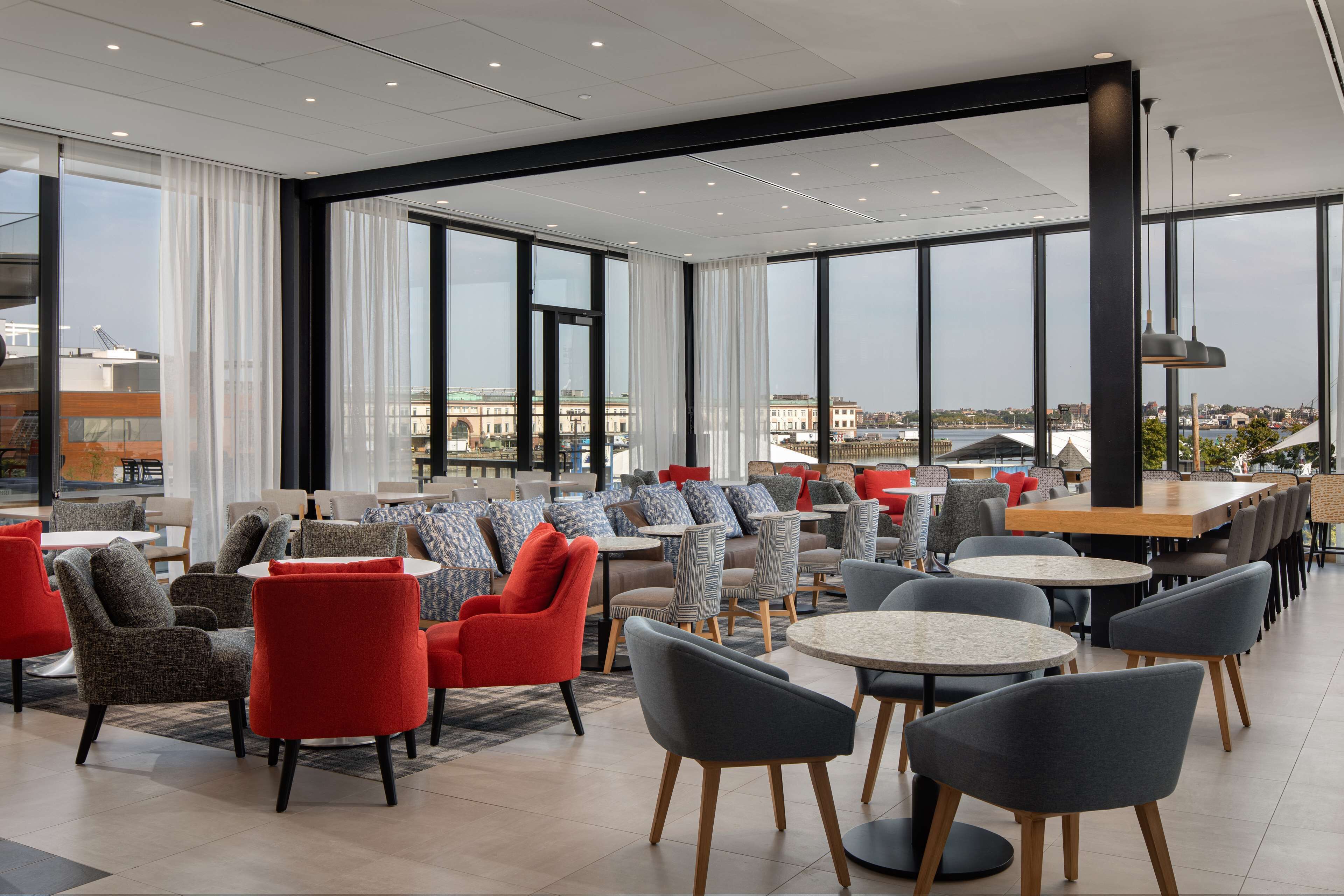 A modern cafe with round tables and chairs, large windows with curtains, and a view of the cityscape.