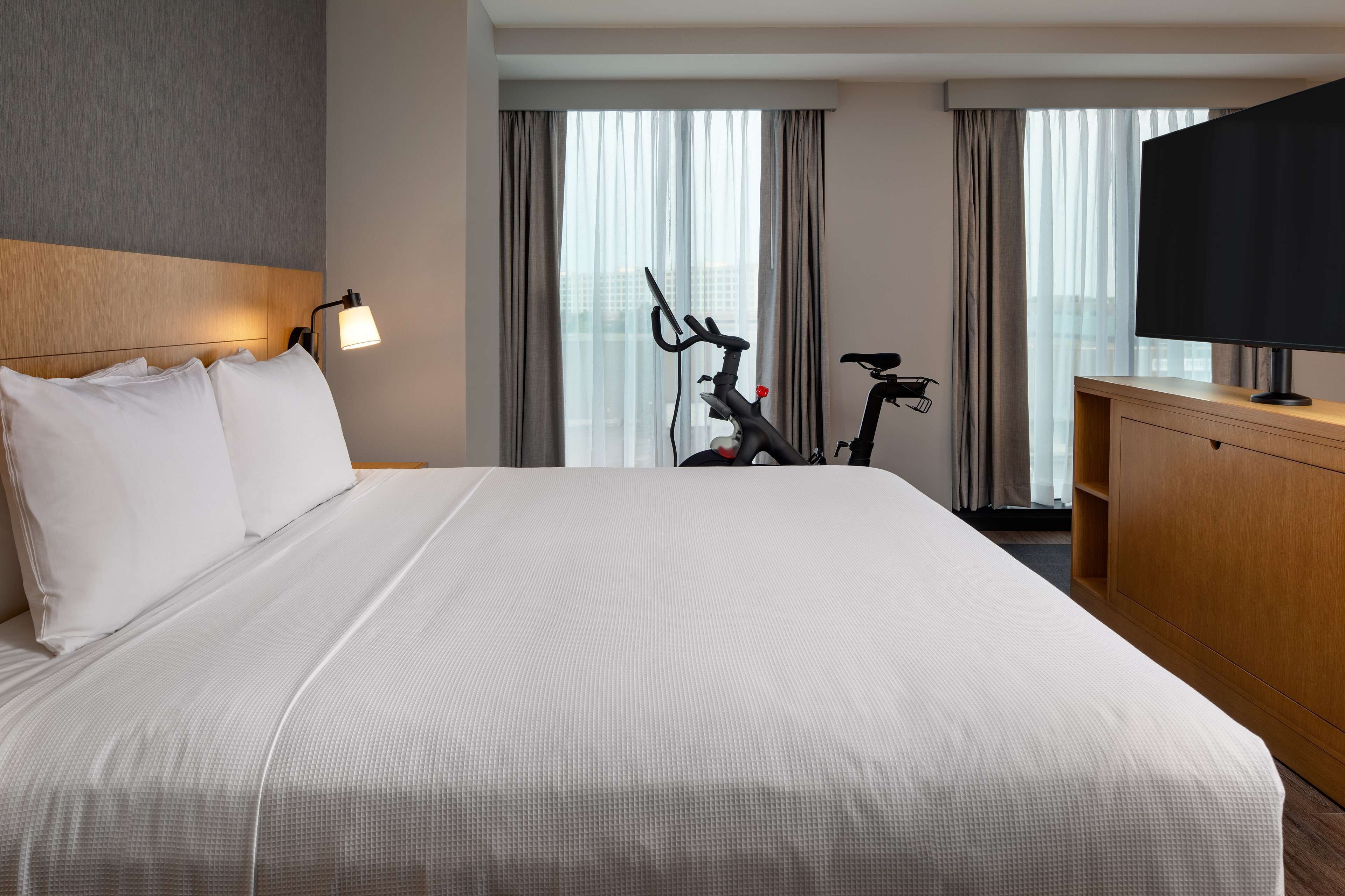 A hotel room with a large bed, a TV, a bike, and a city view.