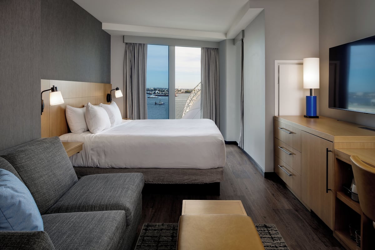 A hotel room with a bed, a sofa, a TV, and a view of a body of water.