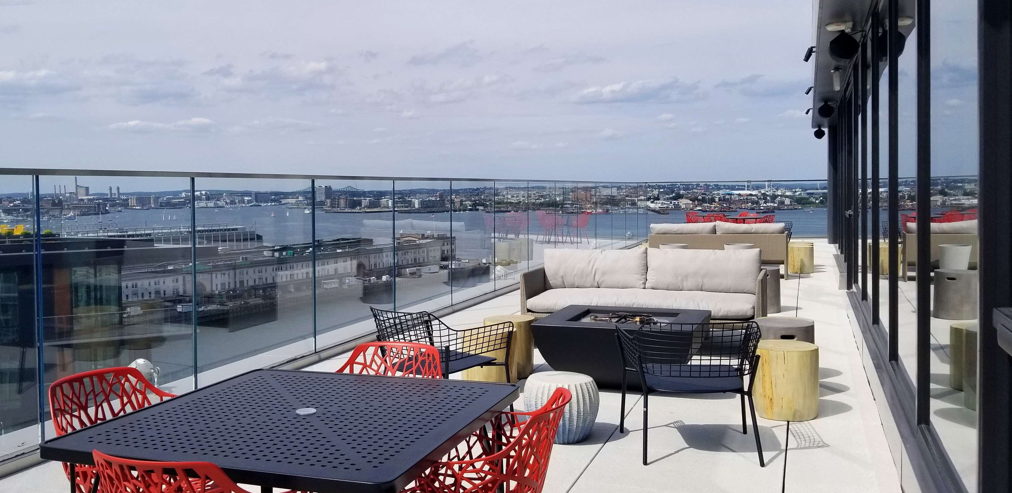 A rooftop terrace with a glass balustrade, outdoor seating, and a view of the cityscape and water.