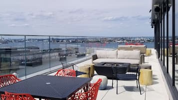 A rooftop terrace with a glass balustrade, outdoor seating, and a view of the cityscape and water.