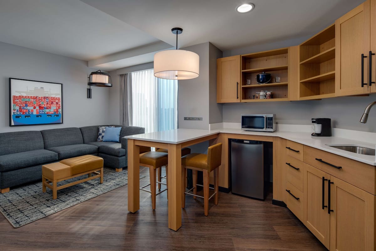 A modern kitchen with wooden cabinets, a dining area with a table and chairs, a built-in microwave, and a large window with curtains.