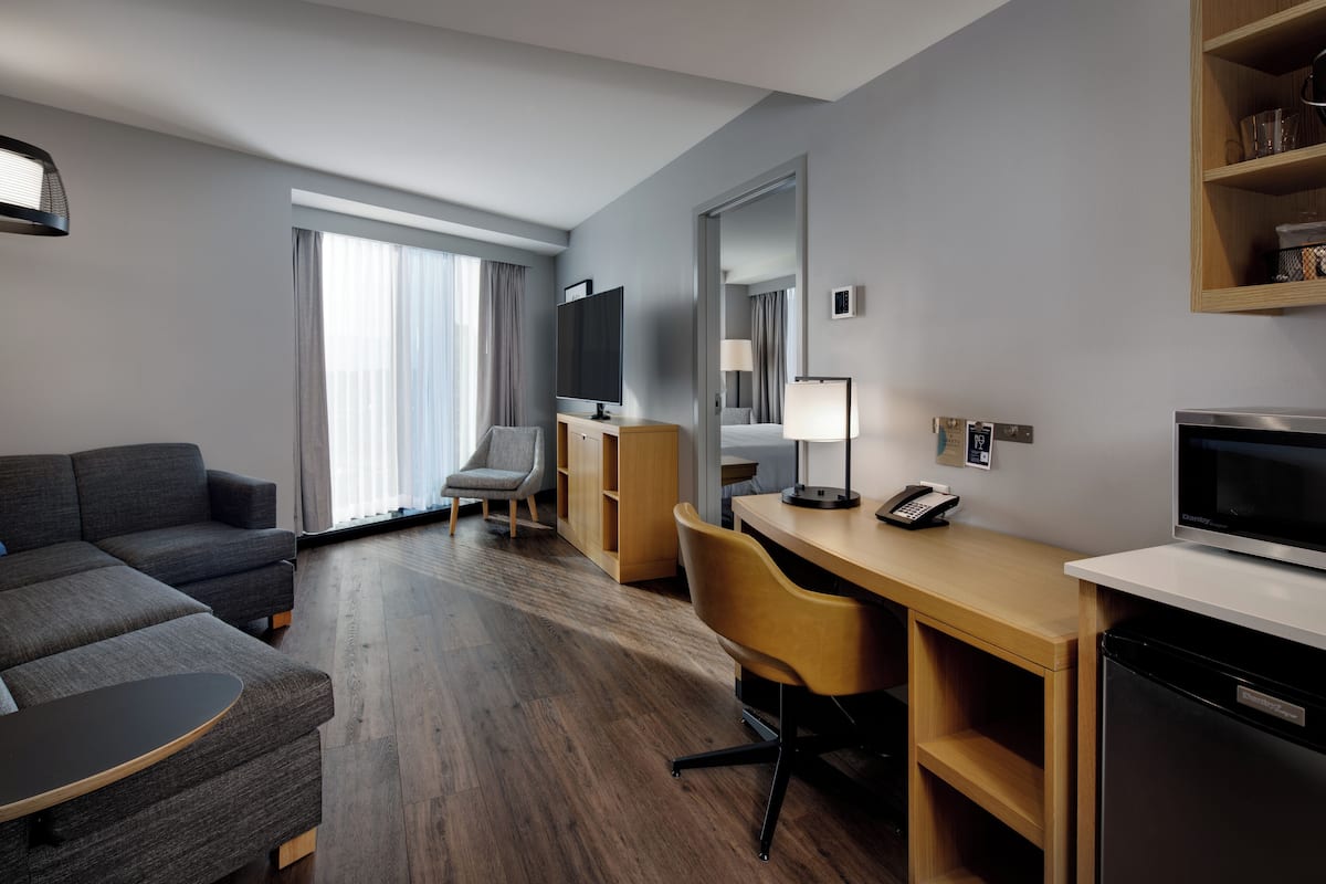A modern hotel room with a sofa, a desk, a television, a lamp, and a microwave.