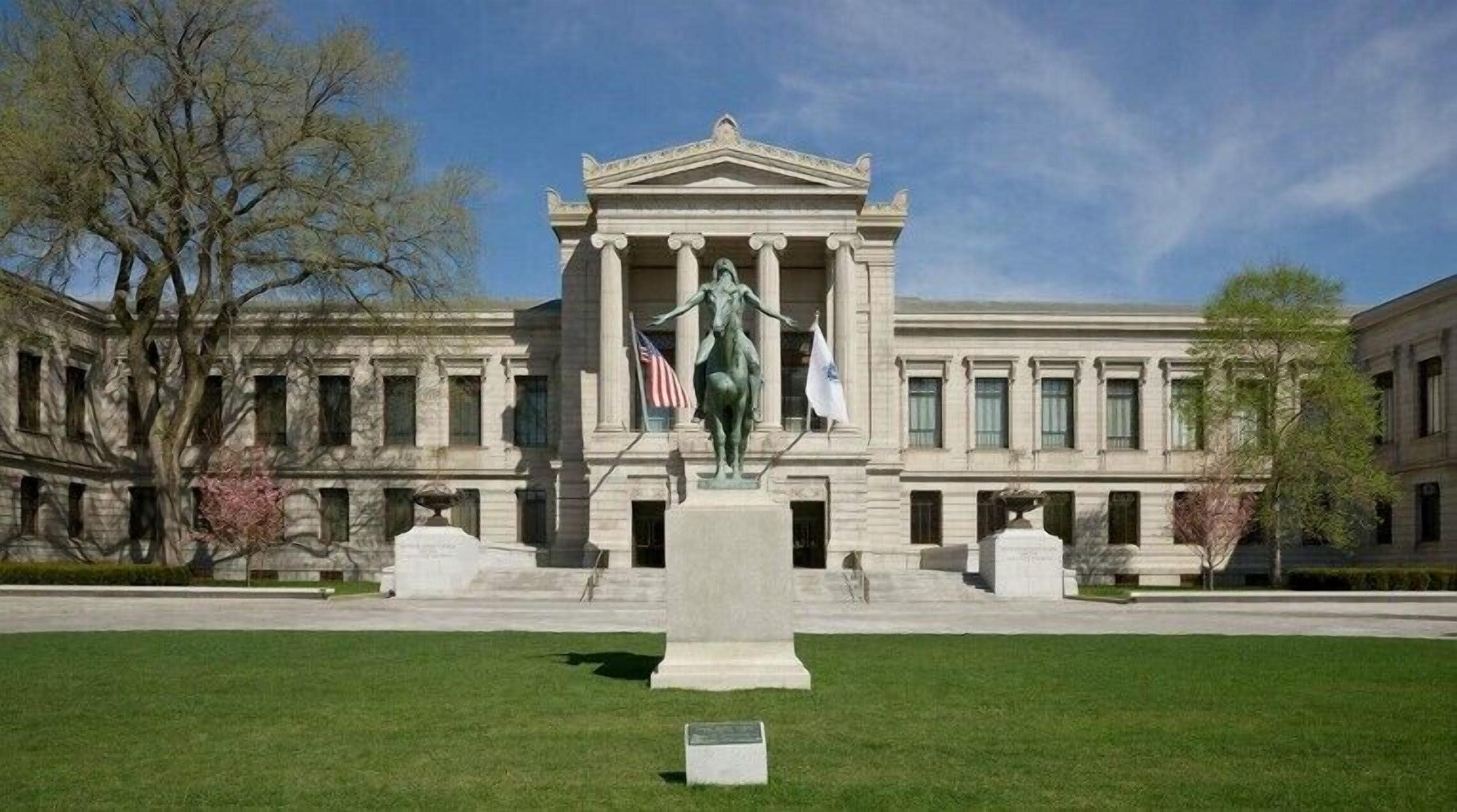 A neoclassical building with a central statue, large windows, and a well-maintained lawn.