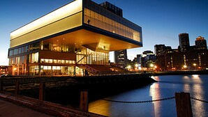 A modern building with a flat roof and large windows, situated by a calm body of water with a chain barrier in the foreground. - Hyatt Place Boston/Seaport District (Boston)