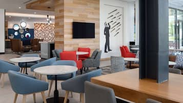 A modern lounge area with round tables and chairs, a flat-screen TV mounted on the wall, and a unique wall art piece.