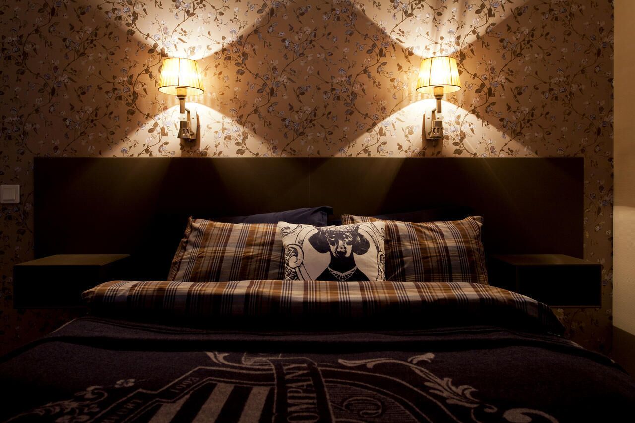 Un dormitorio con cama, dos lámparas de pared y papel tapiz con motivos florales.