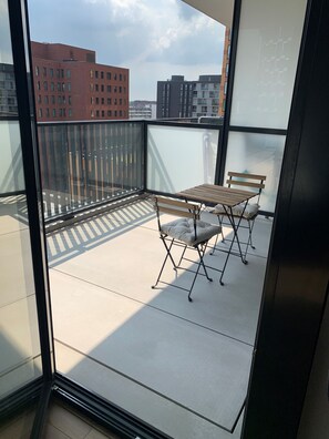 A balcony with a table and chairs, a glass door, and a view of buildings in the background. - Pretty two-room apartment (Suresnes)