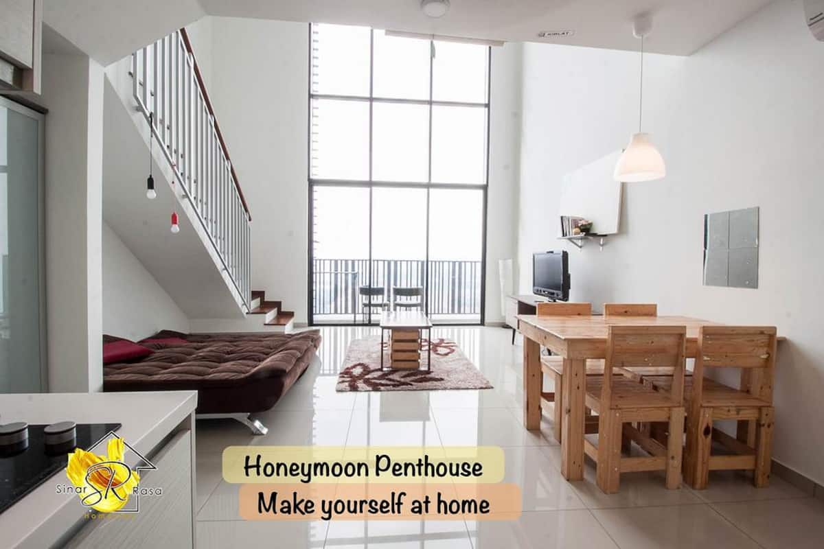 A spacious living area with a staircase, a dining table with chairs, a sofa, and a TV.