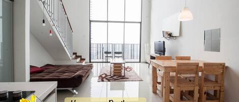 A spacious living area with a staircase, a dining table with chairs, a sofa, and a TV.