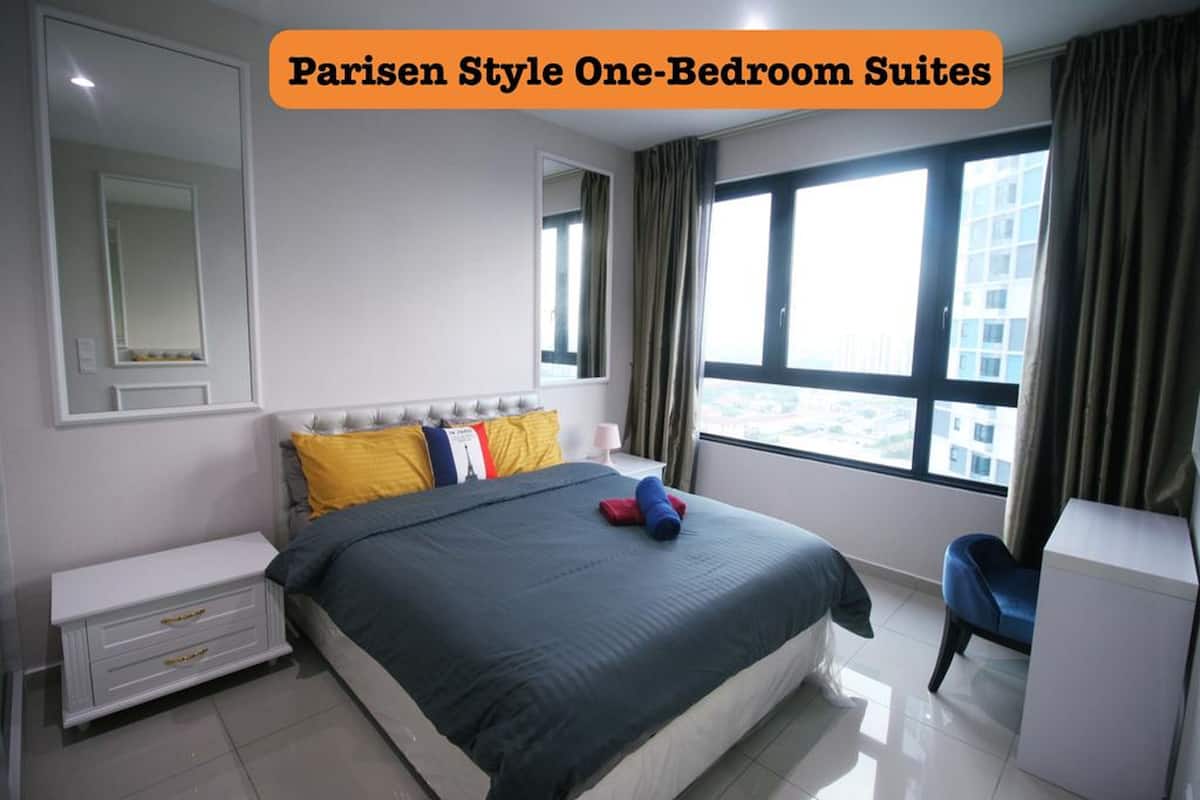 A one-bedroom suite with a bed, bedside table, chair, and large windows.