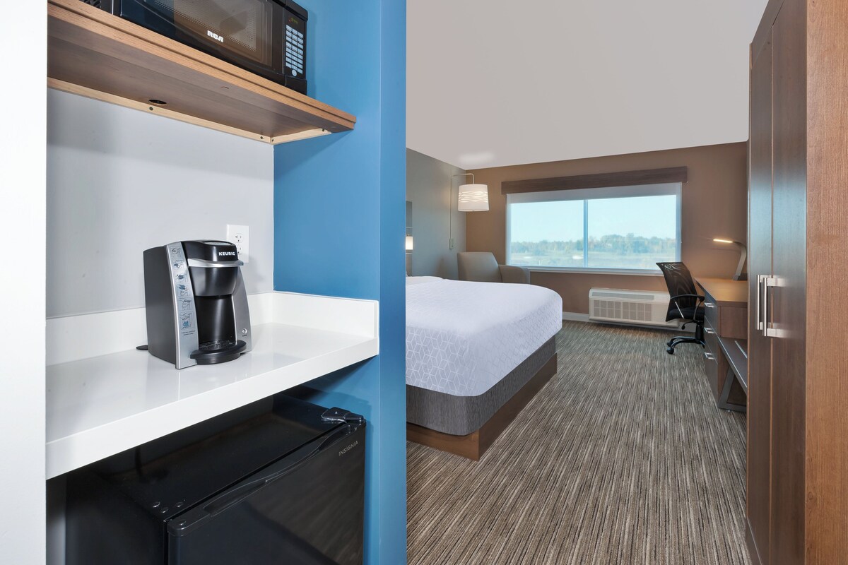 Quarto de hotel com cama, escrivaninha, máquina de café, micro-ondas e janela com vista.