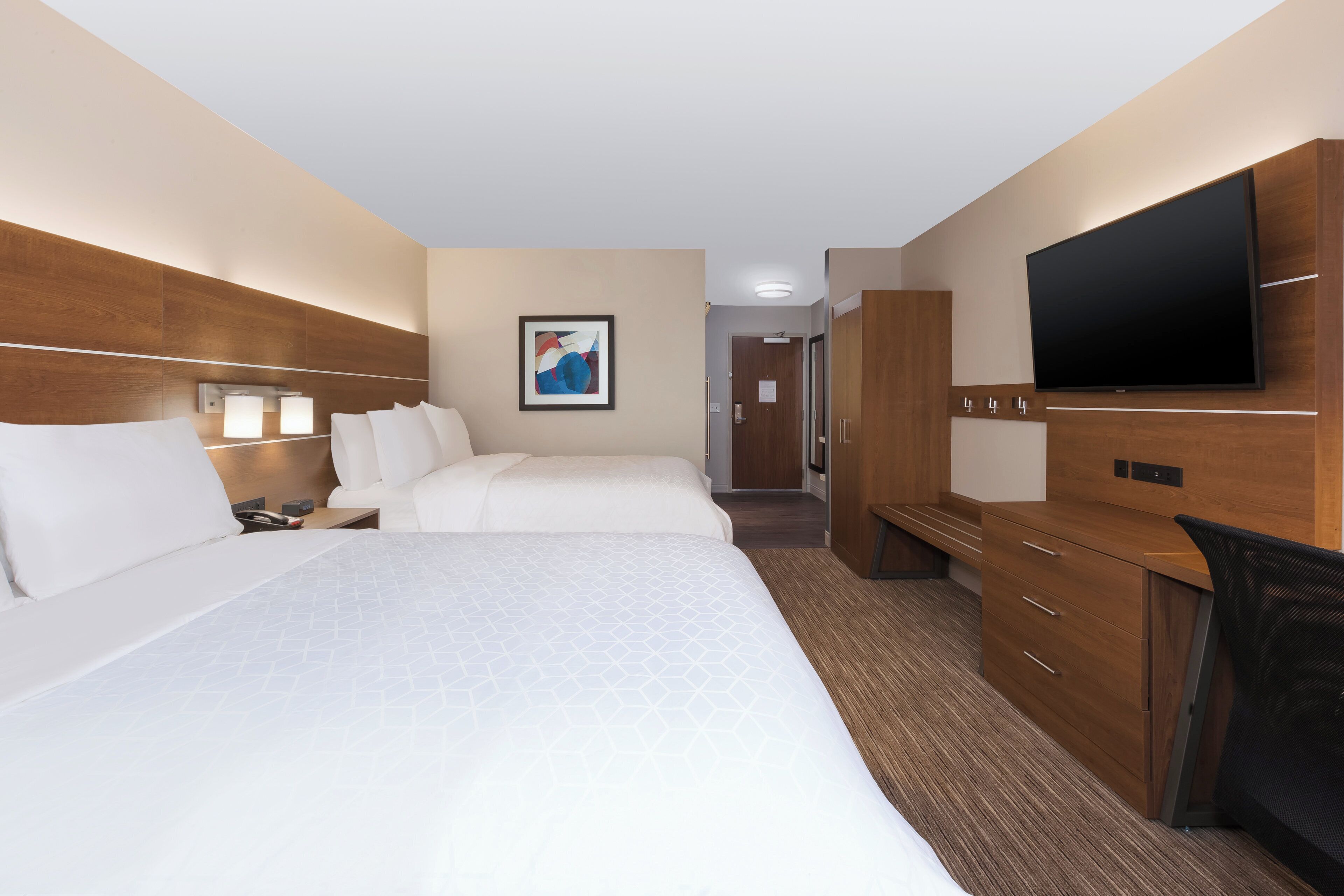 A hotel room with a large bed, a desk, a TV, and a wardrobe.