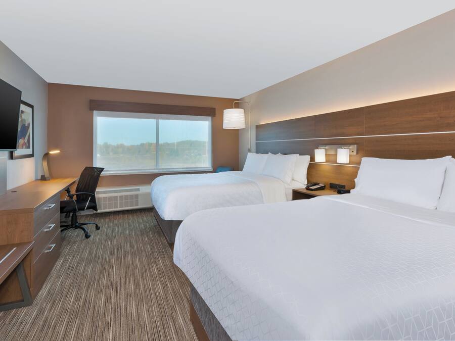 A hotel room with two beds, a desk, a chair, a TV, and a large window.