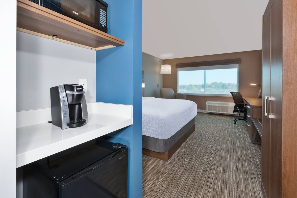 A hotel room with a bed, a desk, a chair, a coffee maker, and a microwave.