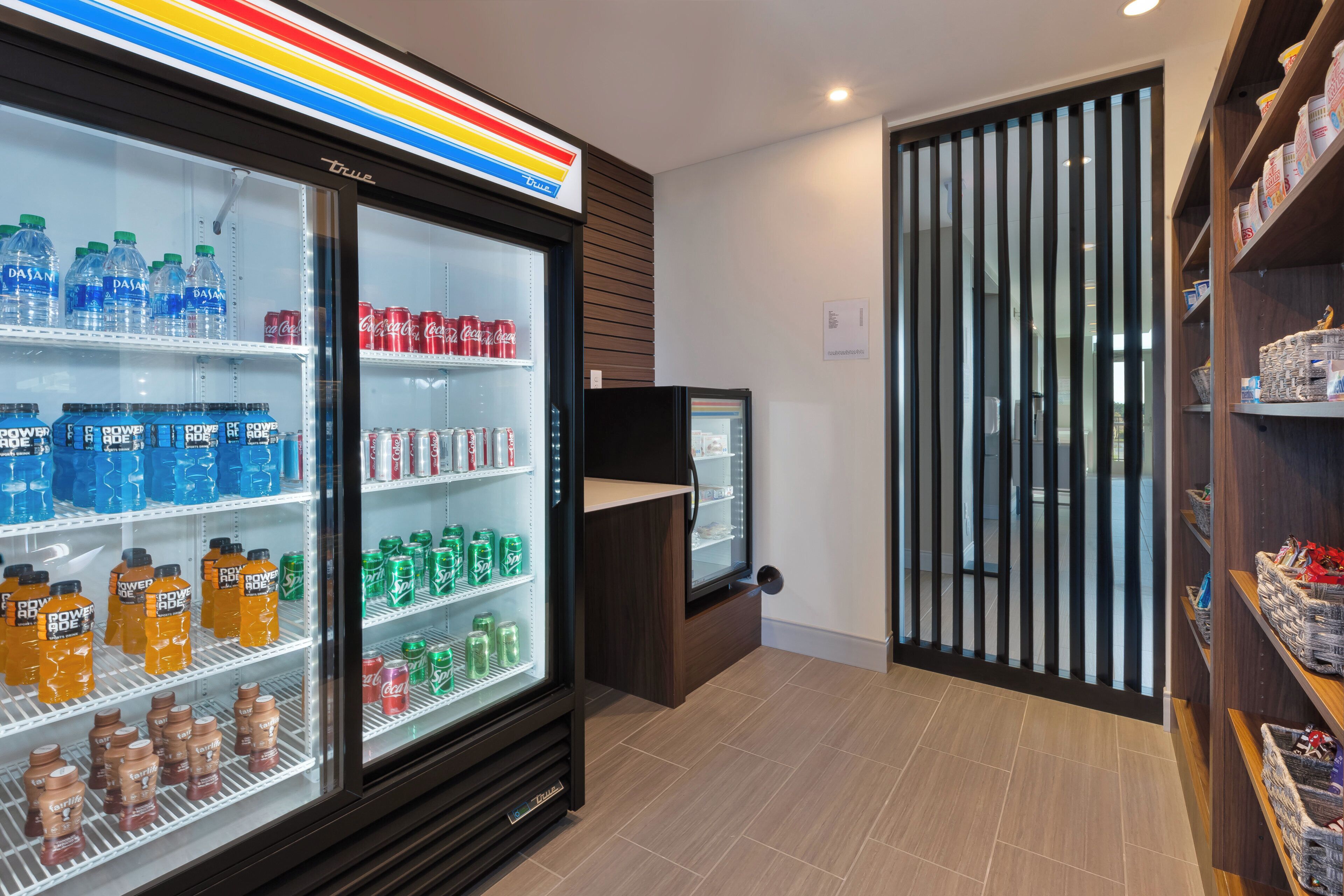 Un refrigerador para bebidas repleto de diversas opciones, una pequeña vitrina expositora y piso de madera.