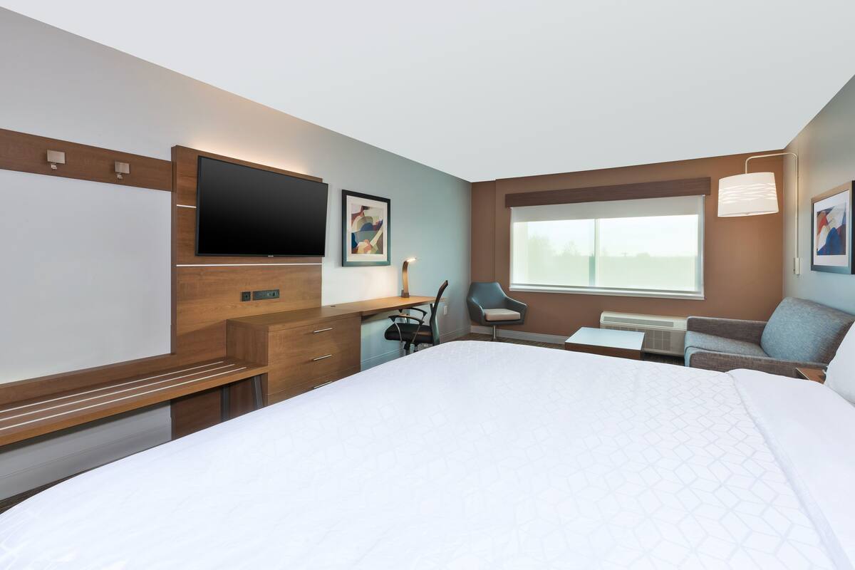 A hotel room with a large bed, a desk with a chair, a flat-screen TV, and a window with a view.