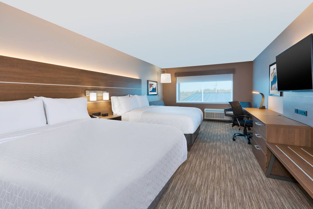 A hotel room with two beds, a desk, a chair, and a TV.