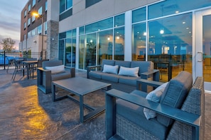 An outdoor seating area with tables and sofas, a stone pillar, and large windows. - Holiday Inn Express & Suites Cedar Springs – Grand Rapids N by IHG (Cedar Springs)