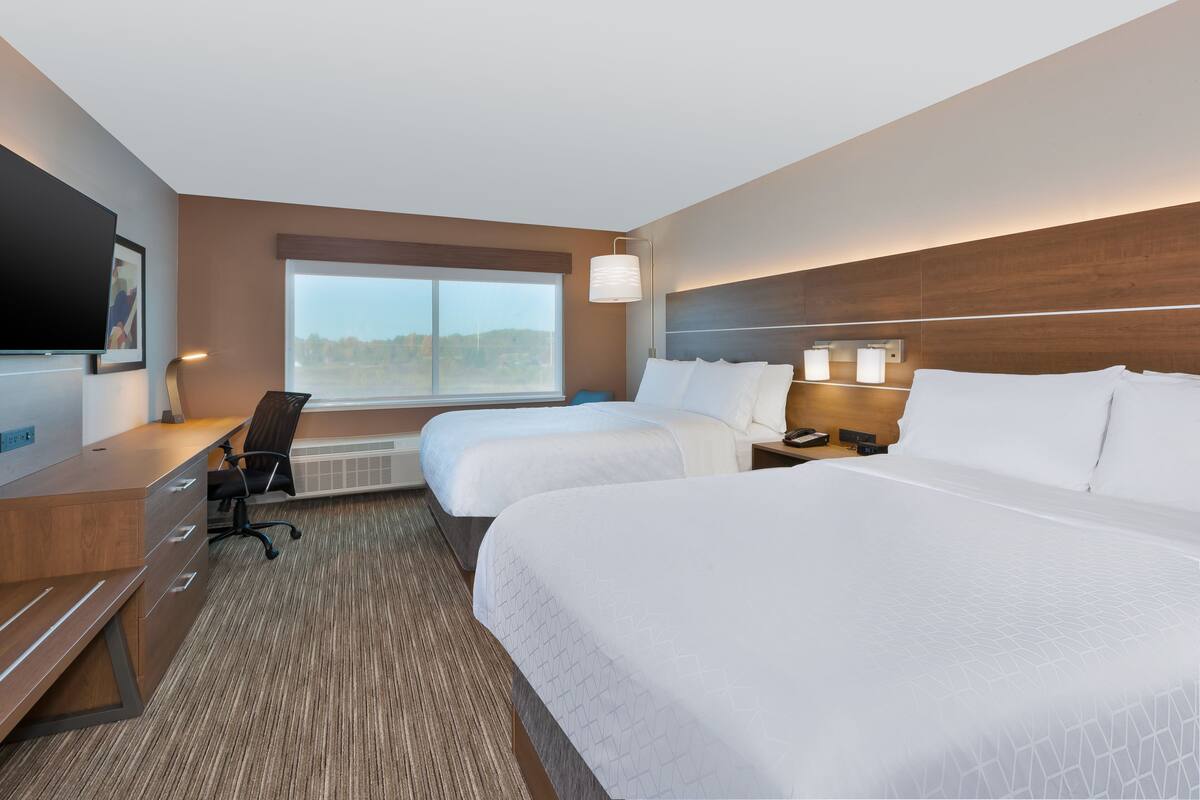 A hotel room with two beds, a desk, a chair, a TV, and a large window.