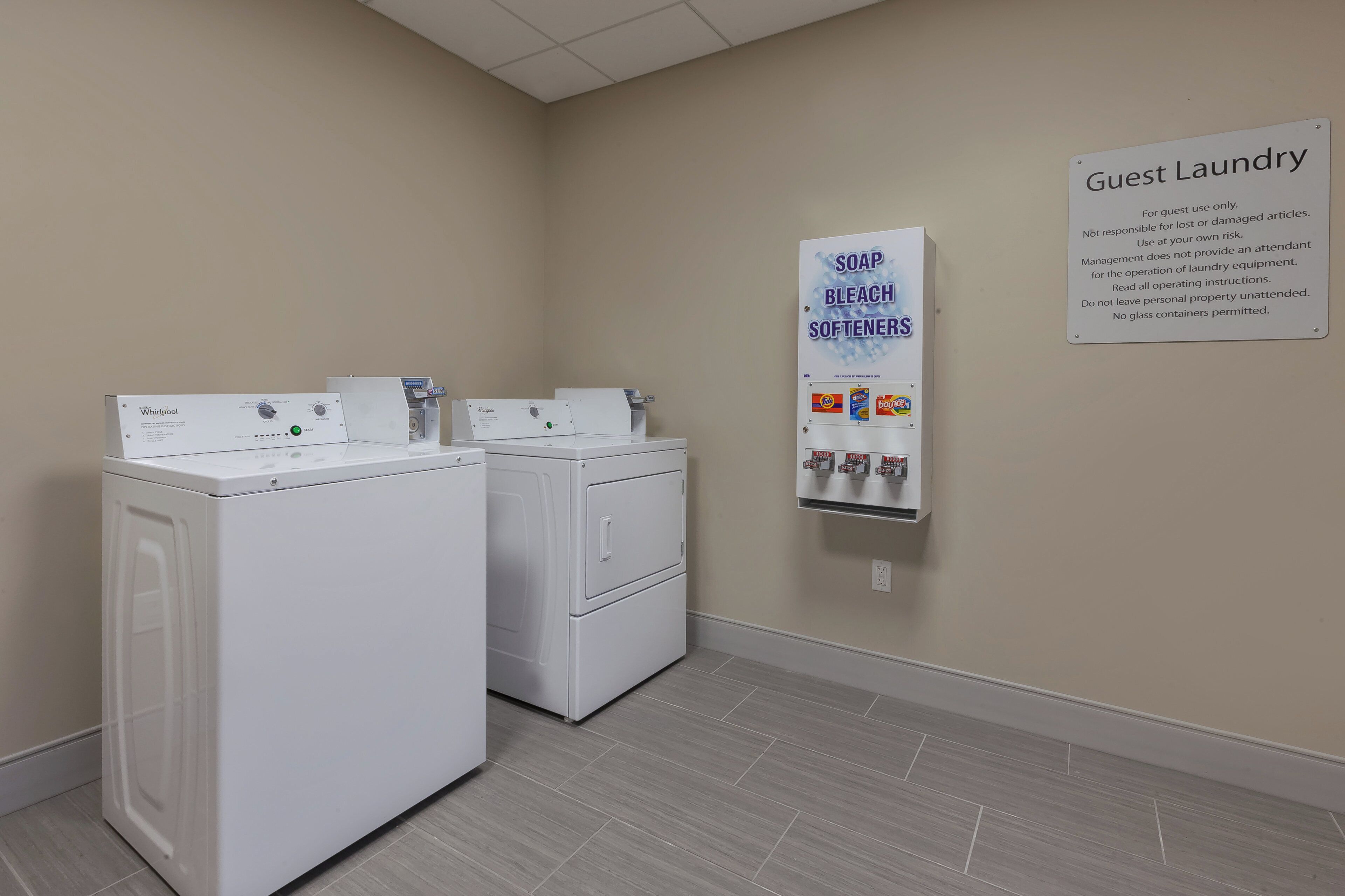 A guest laundry area with Whirlpool washers and dryers, a soap, bleach, and softener dispenser, and a sign with usage instructions.