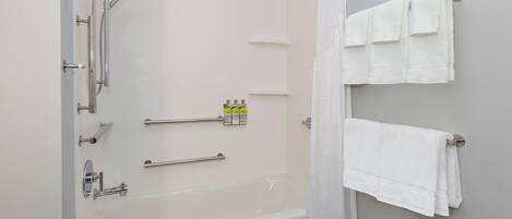 Une salle de bain équipée d’une baignoire, d’une douche et de barres d’appui. On y trouve des serviettes sur un porte-serviettes et un rideau de douche.