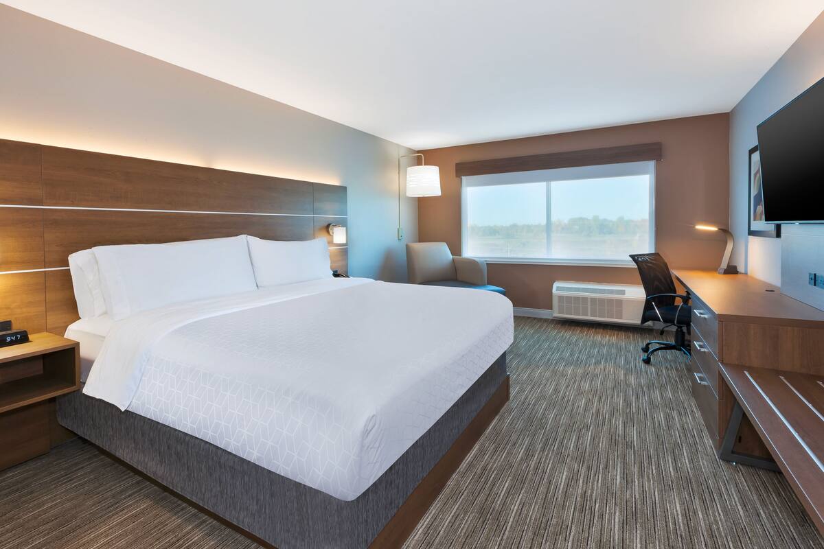 A hotel room with a large bed, a desk, a chair, a TV, and a window with a view.