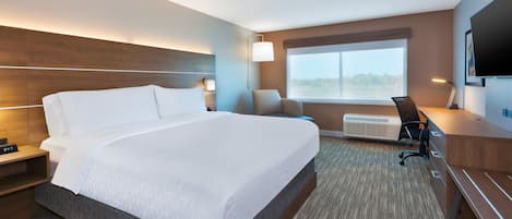 A hotel room with a large bed, a desk, a chair, a TV, and a window with a view.